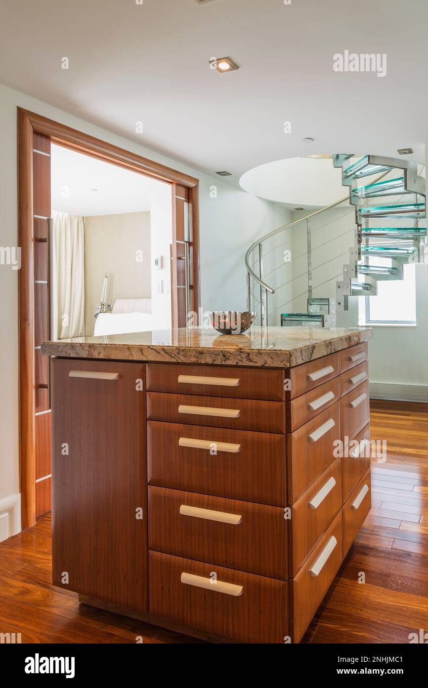 Nuanced granite top exotic wood dresser plus steel and tempered glass spiral staircase in hallway of master bedroom inside modern luxurious condo. Stock Photo