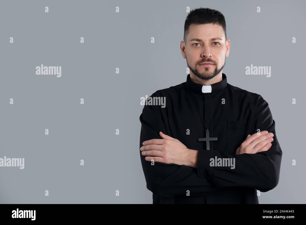 Priest with cross on grey background, space for text Stock Photo
