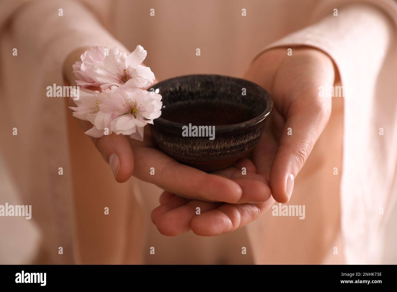 Master holding cup of freshly brewed beverage and sakura flowers during traditional tea ceremony