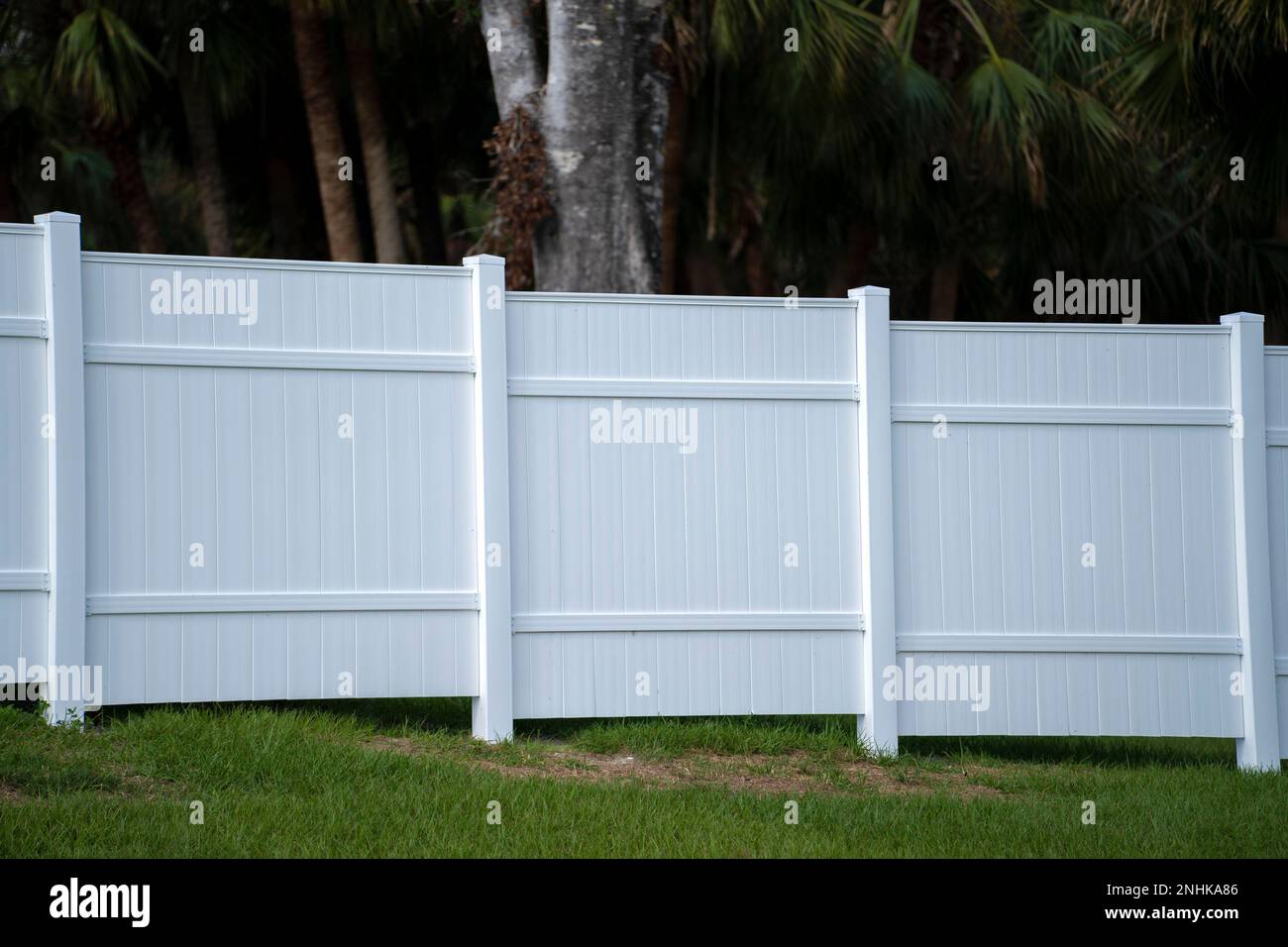 White vinyl picket fence on green lawn surrounding property grounds for backyard protection and privacy Stock Photo