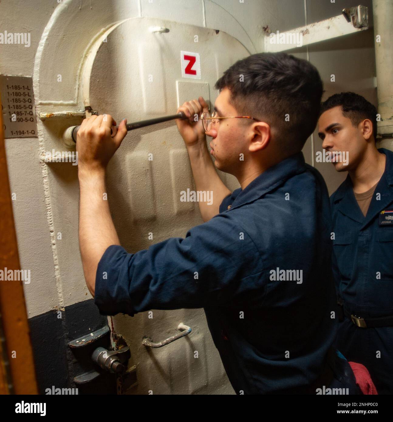 220801-N-YQ181-1015 PHILIPPINE SEA (Aug. 1, 2022) Aerographer’s Mate Airman Apprentice Melvin Thimlar, left, from Middlebury, Indiana, and Logistics Specialist Seaman Joshua Rivera, from Midlothian, Virginia, conduct maintenance on an air tight door in the hangar bay of the U.S. Navy’s only forward-deployed aircraft carrier USS Ronald Reagan (CVN 76) while underway in the Philippine Sea, Aug. 1. Ronald Reagan’s tiger teams are tasked with ensuring the material condition readiness of every door, hatch, scuttle, ladder well, and battle lantern aboard the ship. Ronald Reagan, the flagship of Carr Stock Photo