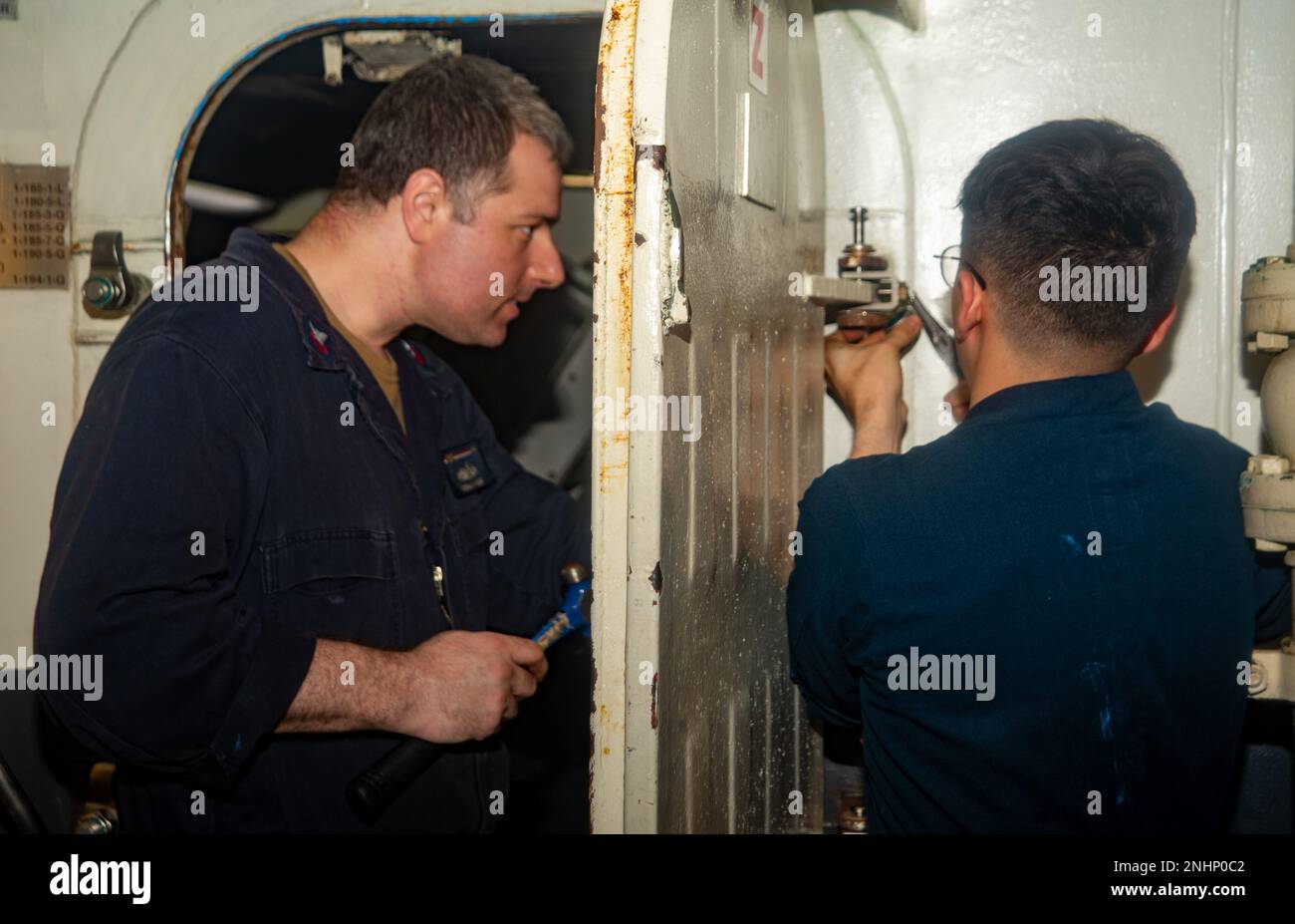 220801-N-YQ181-1049 PHILIPPINE SEA (Aug. 1, 2022) Machinist’s Mate (Nuclear) 1st Class Conrad Warren, left, from Mesa, Arizona, and Aerographer’s Mate Airman Apprentice Melvin Thimlar, from Middlebury, Indiana, conduct maintenance on an air tight door in the hangar bay of the U.S. Navy’s only forward-deployed aircraft carrier USS Ronald Reagan (CVN 76) while underway in the Philippine Sea, Aug. 1. Ronald Reagan’s tiger teams are tasked with ensuring the material condition readiness of every door, hatch, scuttle, ladder well, and battle lantern aboard the ship. Ronald Reagan, the flagship of Ca Stock Photo