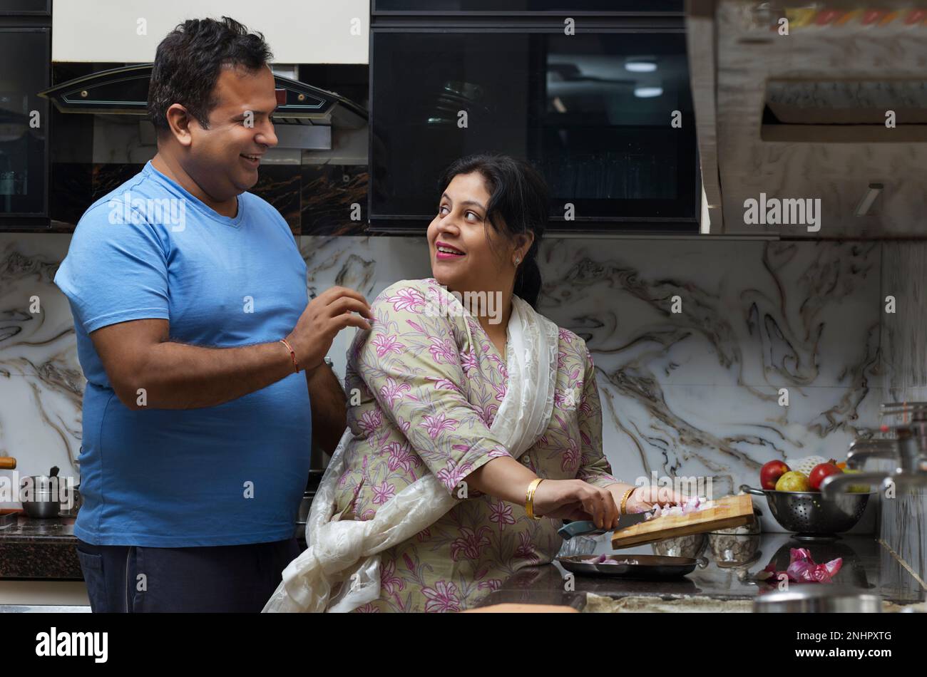 Portrait of woman chopping onion and husband standing behind in kitchen Stock Photo