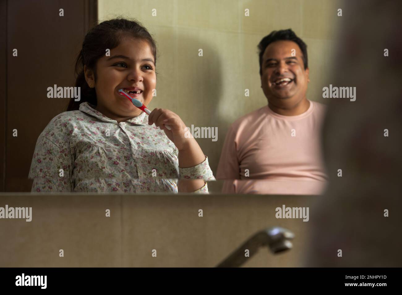 Portrait of little girl brushing teeth and father standing beside Stock Photo