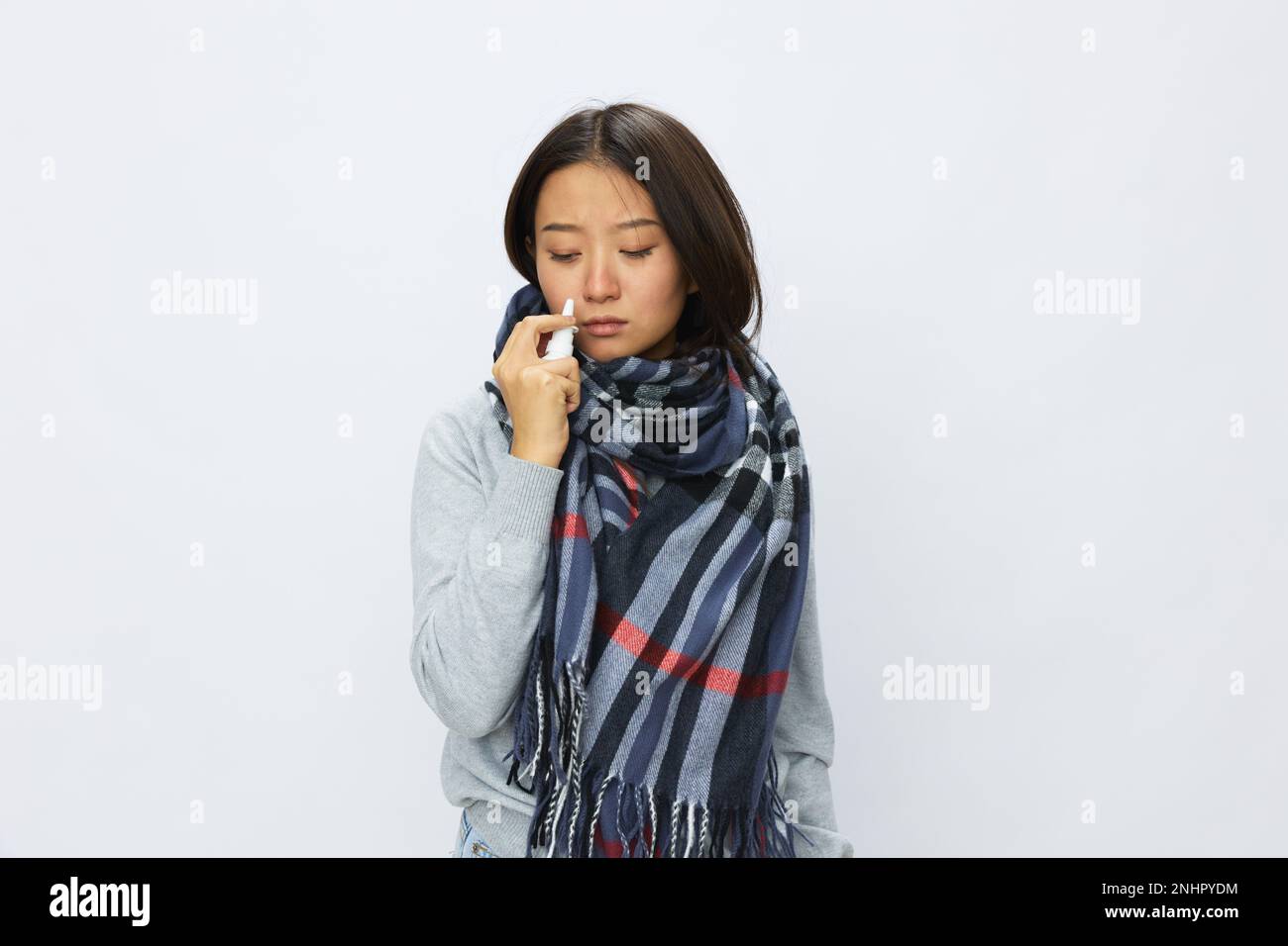 Asian woman flu cold with stuffy nose holds nasal spray and sprays