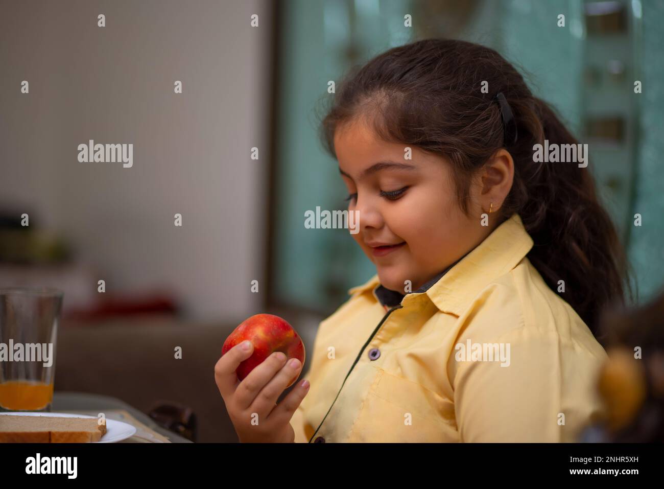 Close-up portrait of little girl while eating apple during breakfast at home Stock Photo