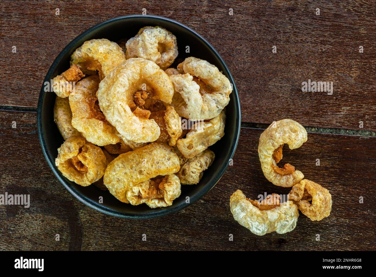 Top view of homemade crispy delicious deep fried pork rinds in black ceramic bowl on wooden
