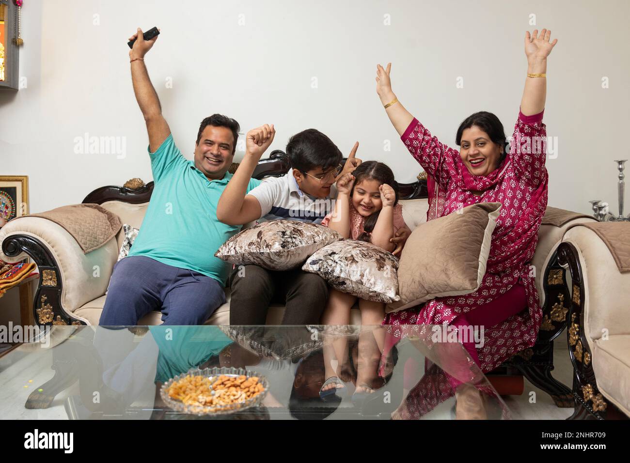 Family cheering while watching TV together in living room Stock Photo