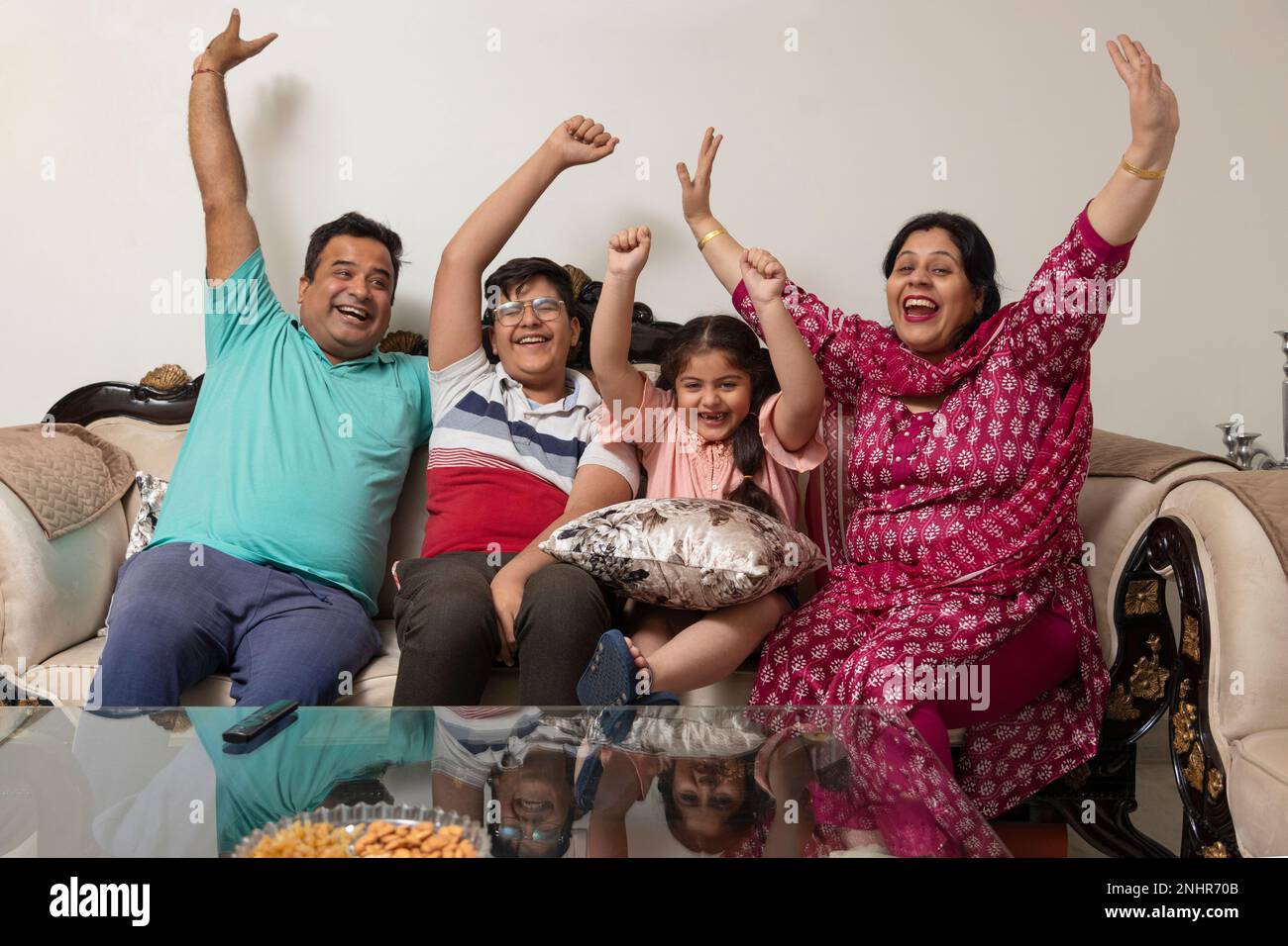 Family cheering while watching TV together in living room Stock Photo