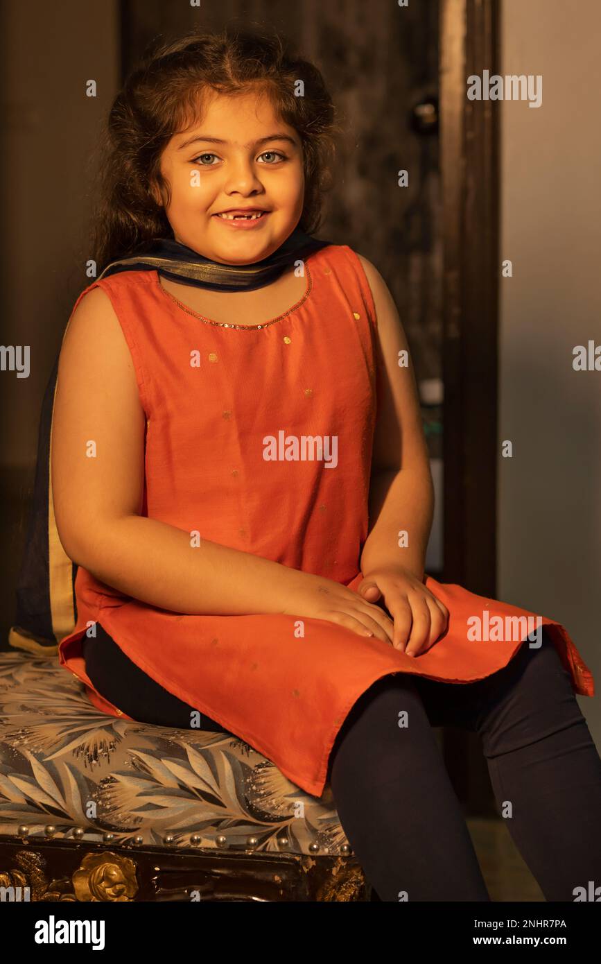 Portrait of smiling little girl sitting on chair at home Stock Photo ...