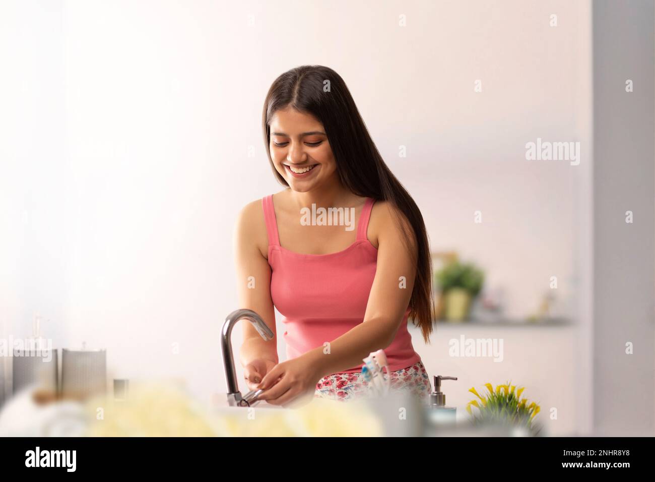 Cheerful young woman washing her hands in bathroom Stock Photo