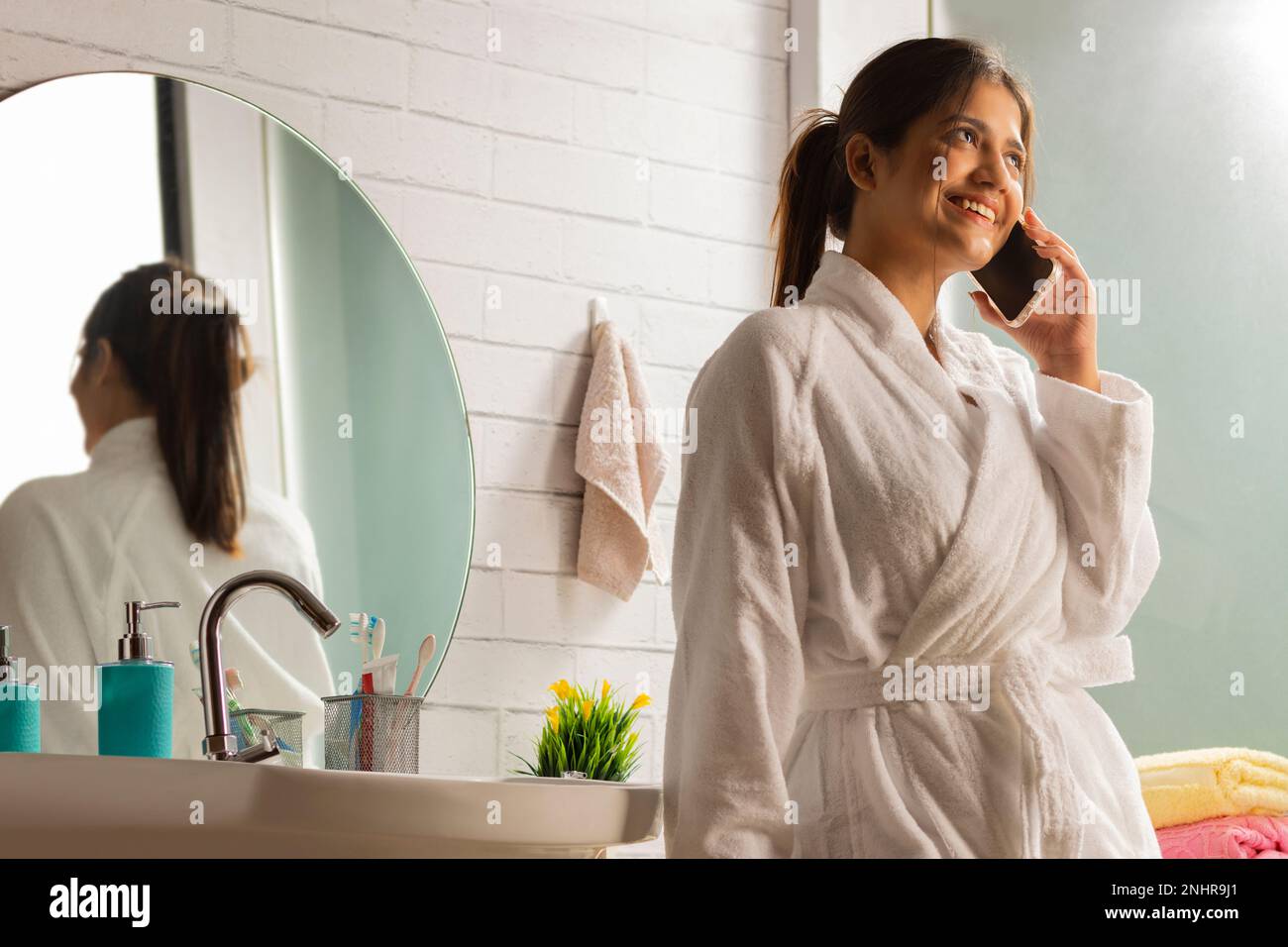 Woman in bathrobes talking on mobile phone in bathroom Stock Photo
