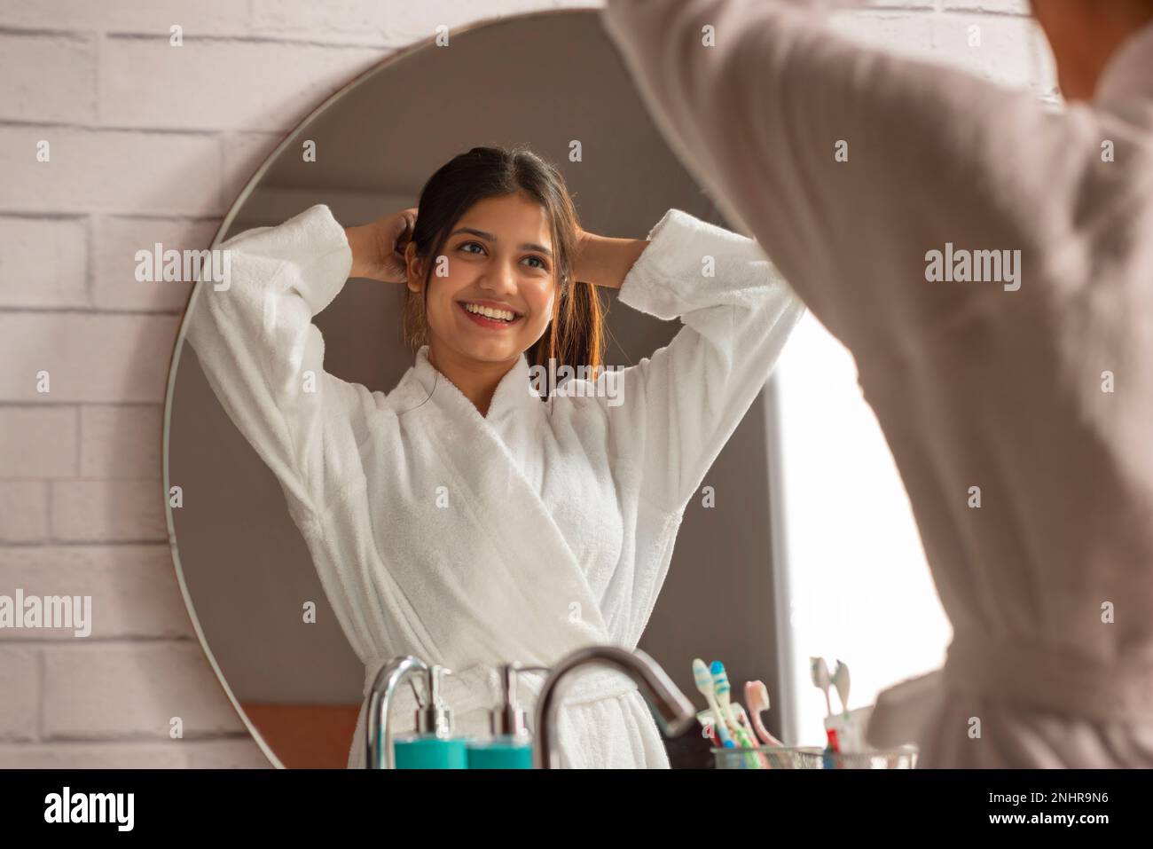 Cheerful woman in bathrobes fixing her hair in bathroom mirror Stock Photo