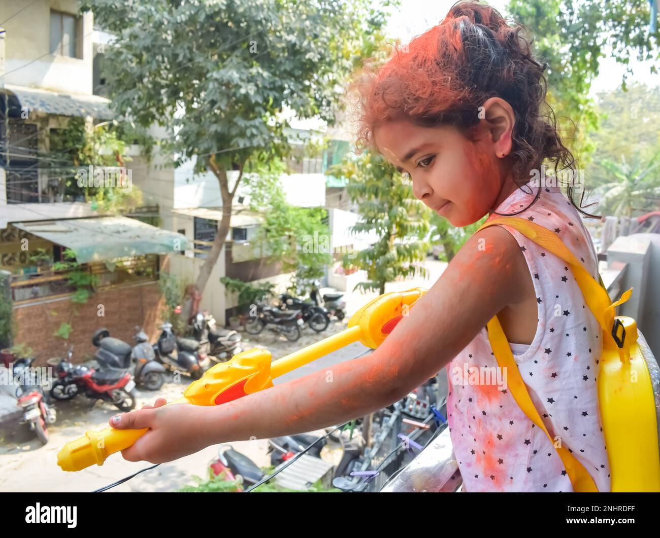 Sweet little Indian girl playing colours on Holi festival, holding pichakaree full of colours, Holi festival celebrations in Delhi, India Stock Photo