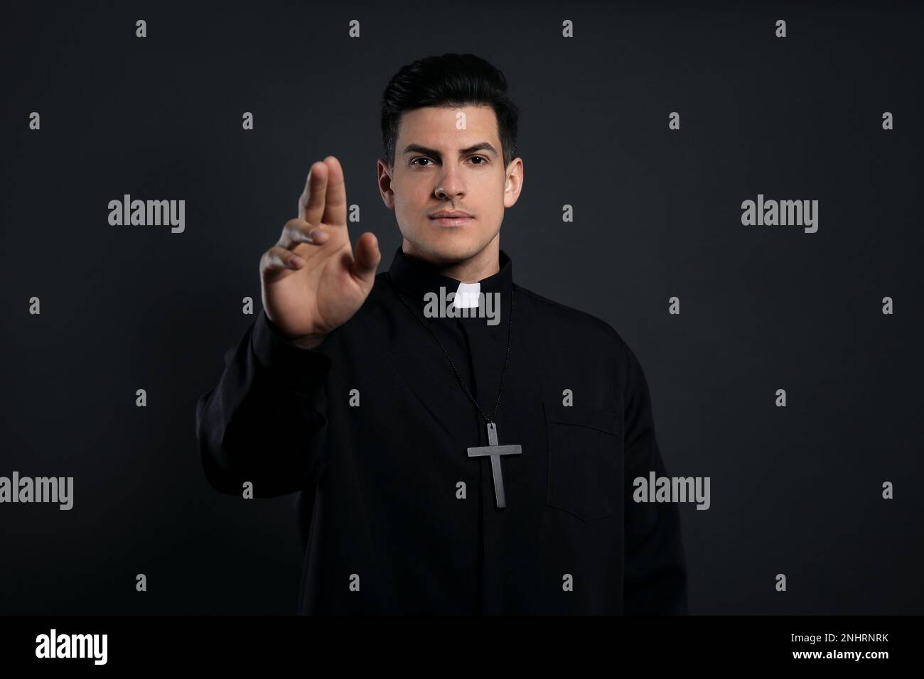 Priest making blessing gesture on black background Stock Photo