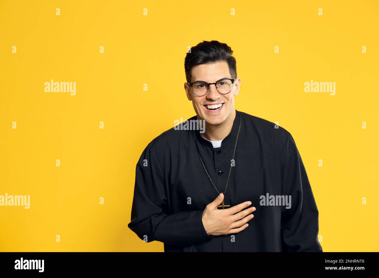 Priest in cassock with clerical collar laughing on yellow background Stock Photo