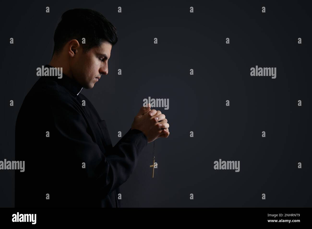 Priest with cross praying on black background. Space for text Stock Photo