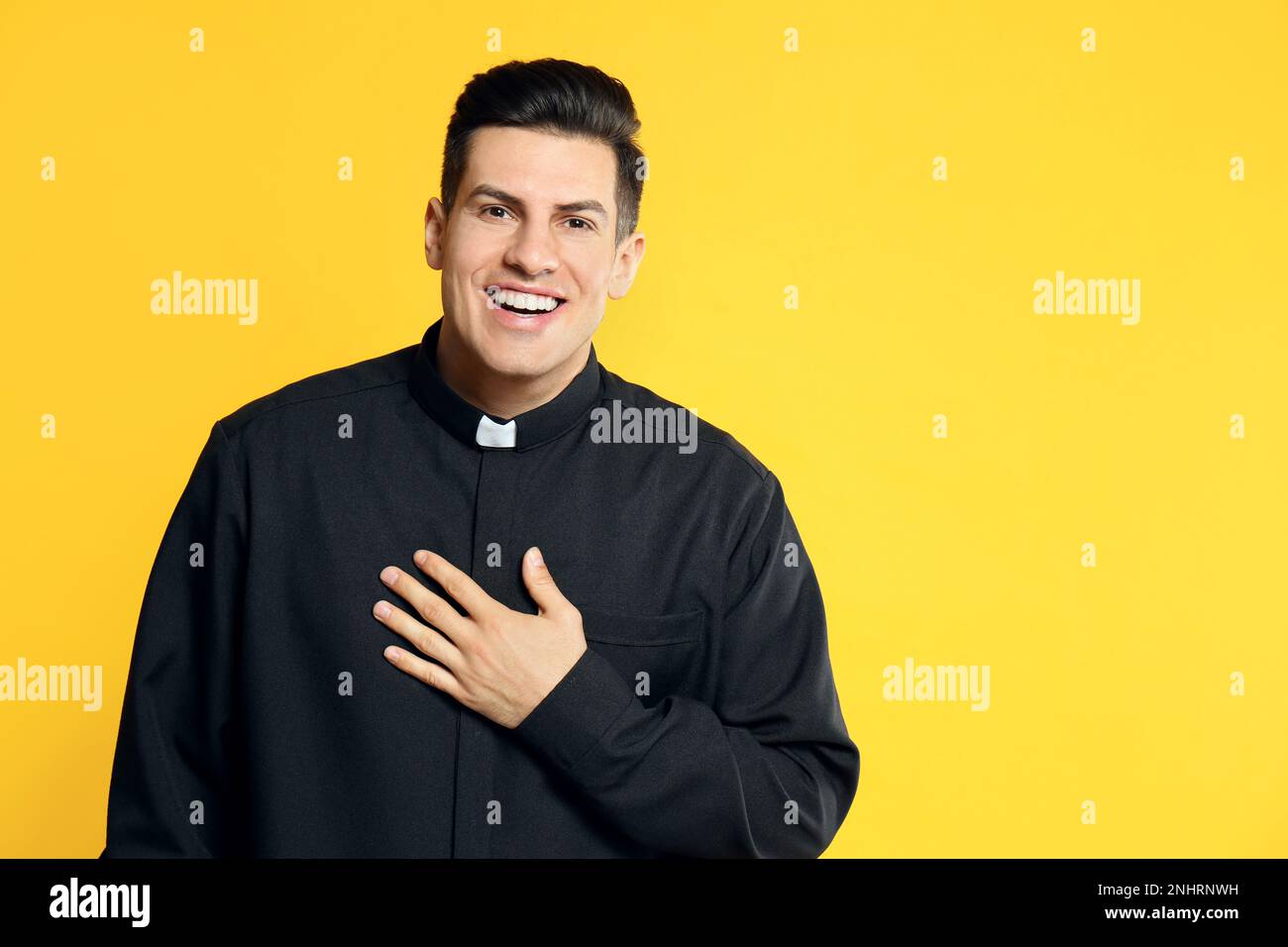 Priest in cassock with clerical collar laughing on yellow background. Space for text Stock Photo