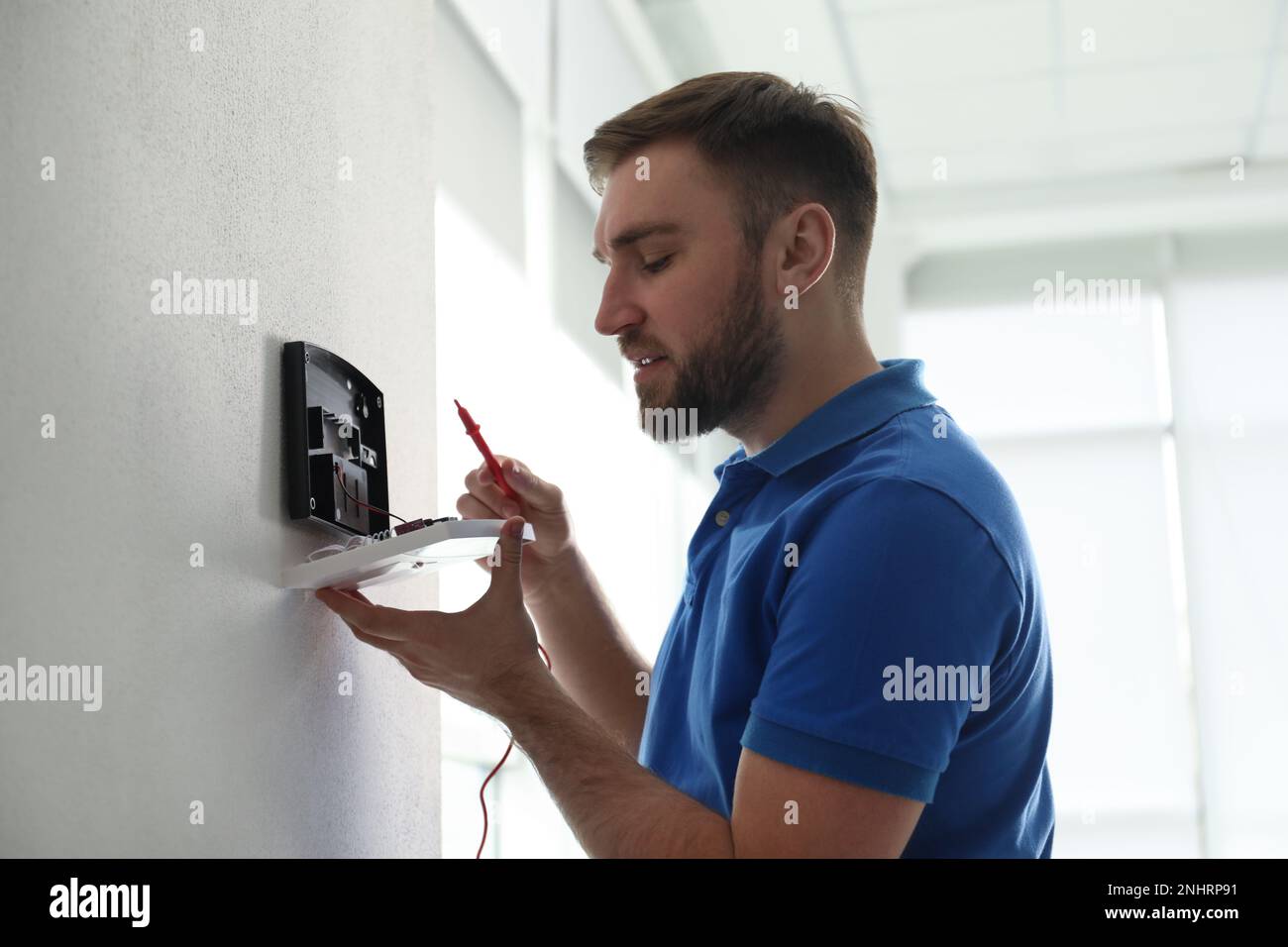 Man installing home security system on white wall in room Stock Photo