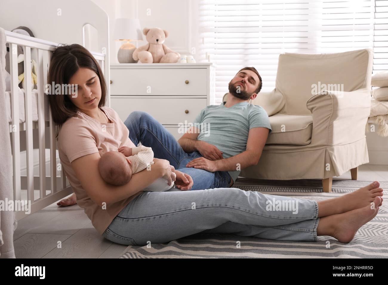 Tired young parents with their baby sleeping on floor in children's