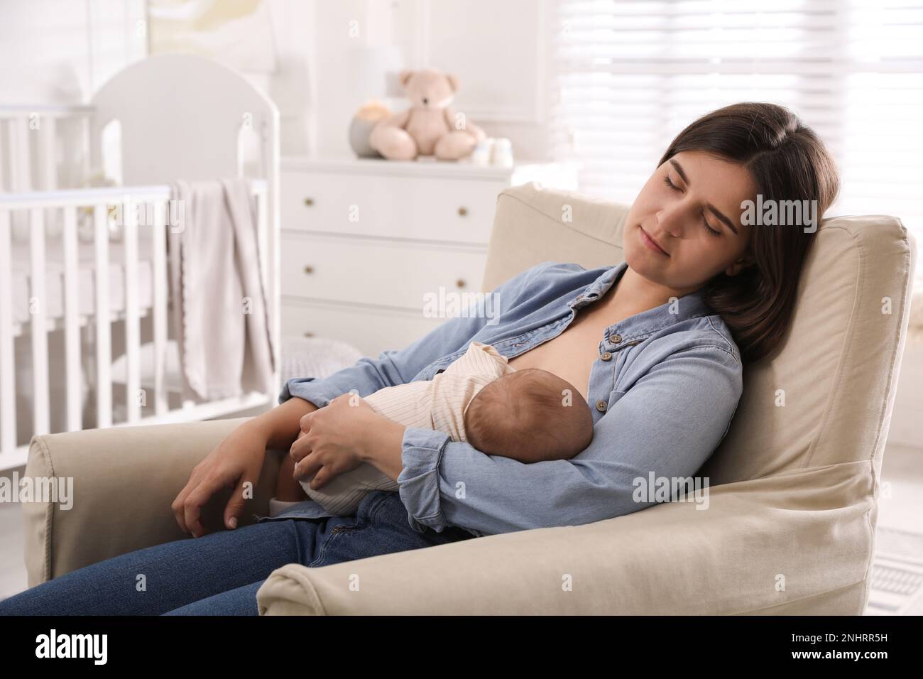 Tired young mother sleeping while breastfeeding her baby in children's
