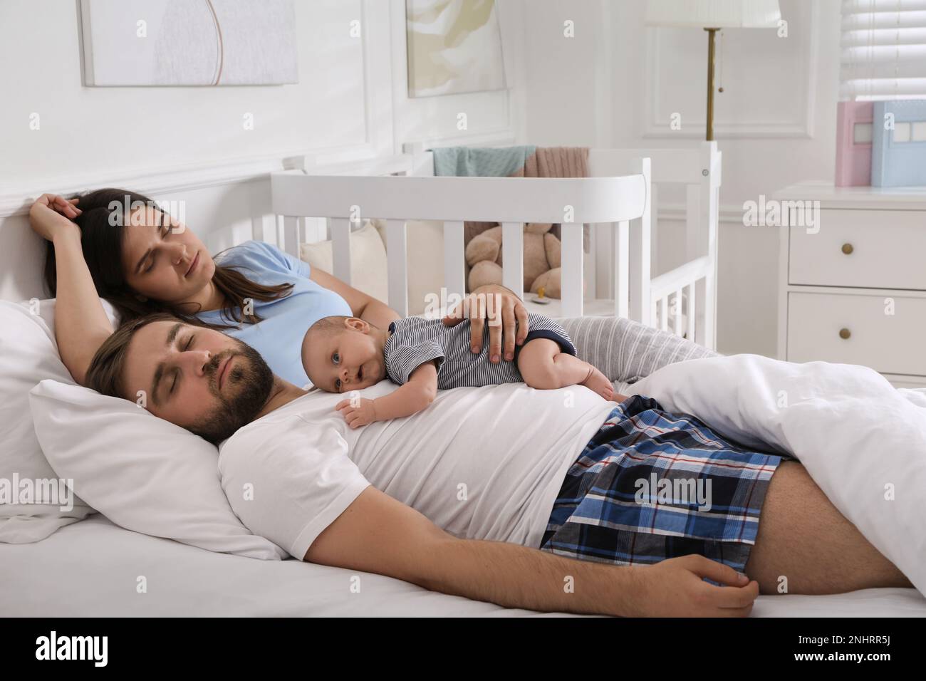 Tired young parents with their baby sleeping in bed at home Stock Photo