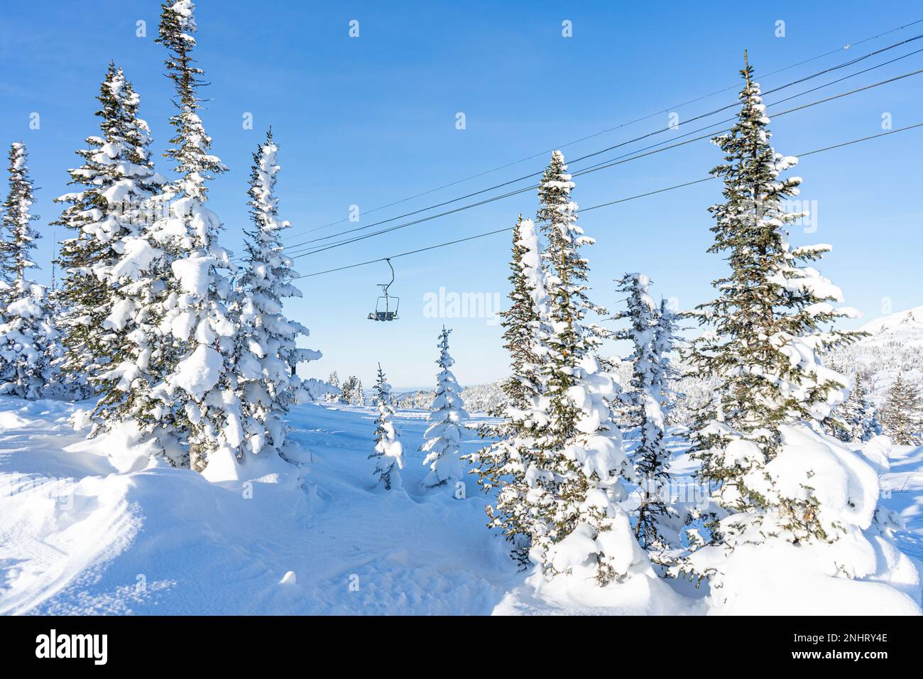 One chair of an empty chair lift in a ski resort at sunny day. Winter holidays, snow-covered coniferous trees Stock Photo
