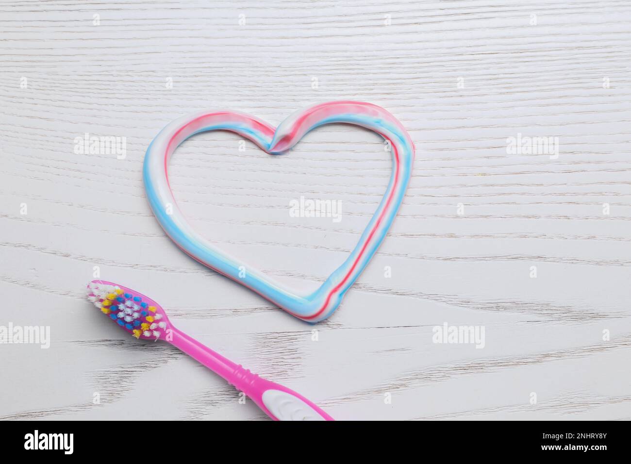 Heart made with toothpaste and brush on white wooden background, flat lay Stock Photo