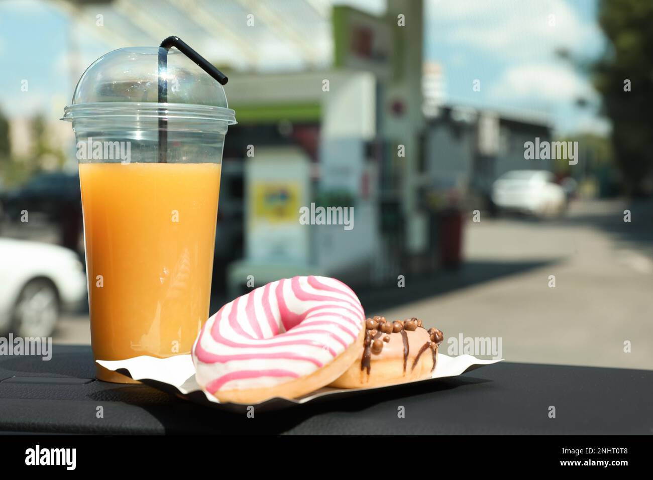 Plastic cup of juice and doughnuts on car dashboard at gas station