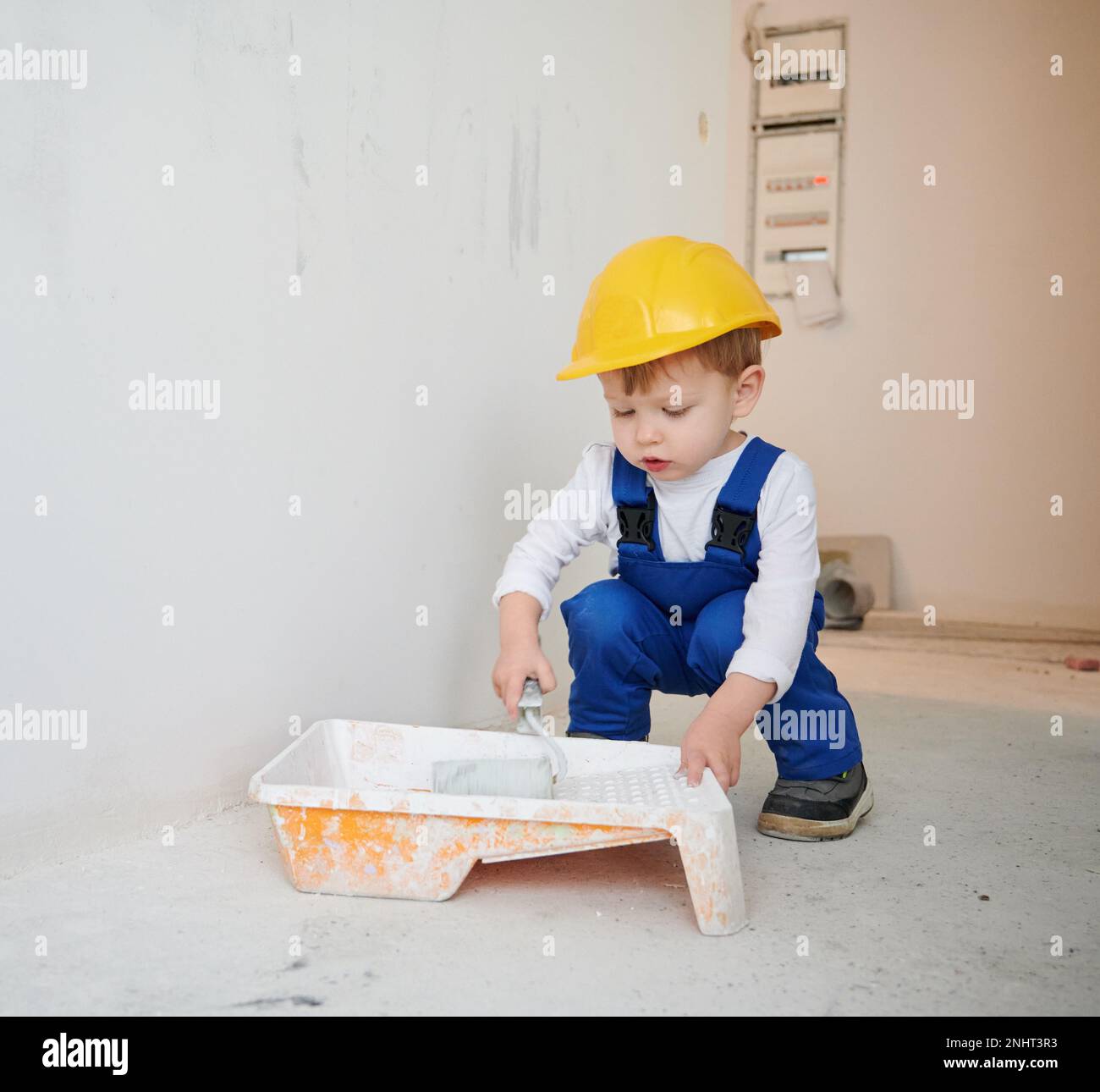 Adorable child construction worker crouching down and preparing paint