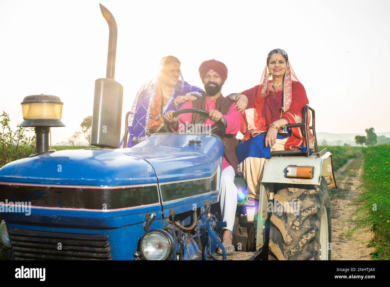 Happy punjabi sikh farmer family driving tractor at agriculture field