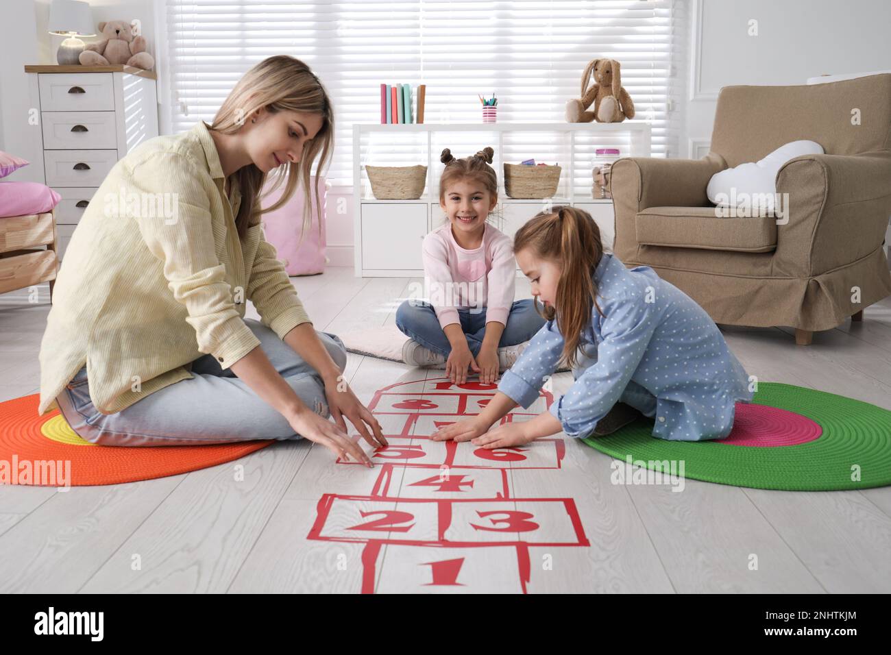 Mother and little girls taping sticker hopscotch on floor at home Stock Photo