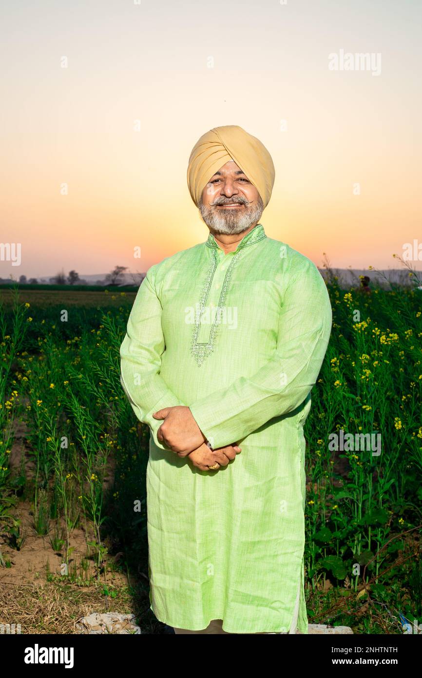 Portrait of happy senior punjabi sikh man standing cross arms wearing turban and kurta looking at camera at agriculture field. Stock Photo