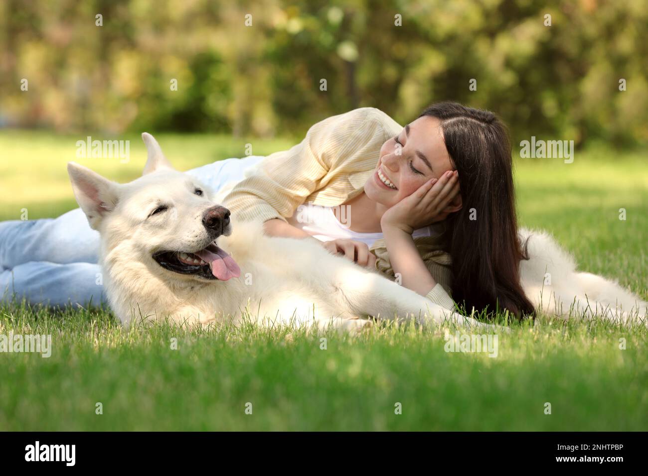 Teenage girl lying with her white Swiss Shepherd dog on green grass in ...
