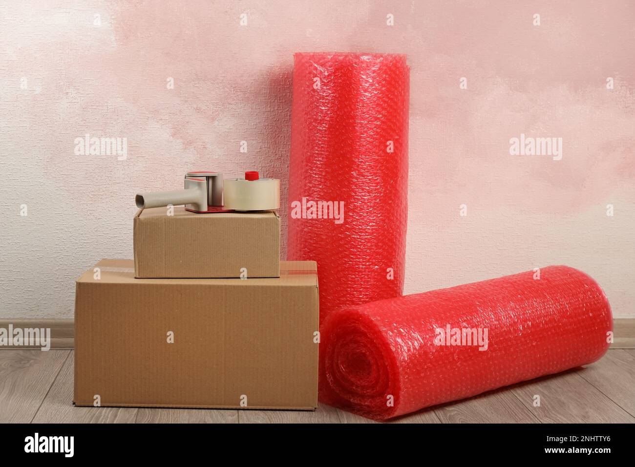 Red bubble wrap rolls, tape dispenser and cardboard boxes on floor near