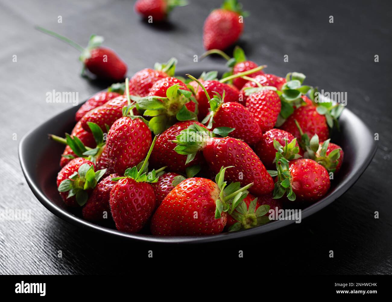 Strawberries in a black plate on dark background Stock Photo - Alamy
