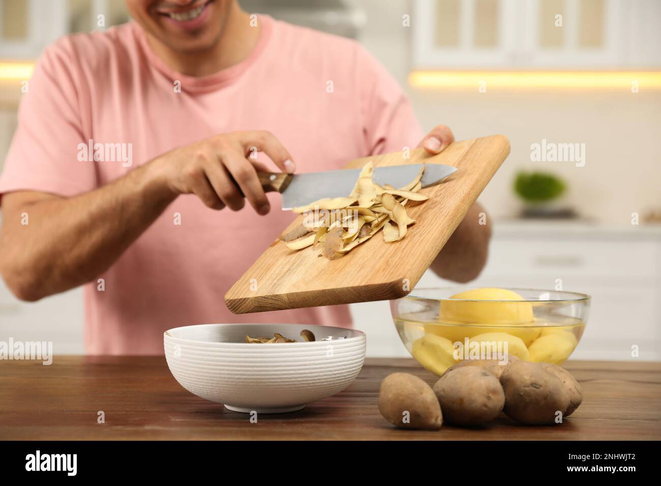 Man with cutting board and knife scraping vegetable peels into bowl on