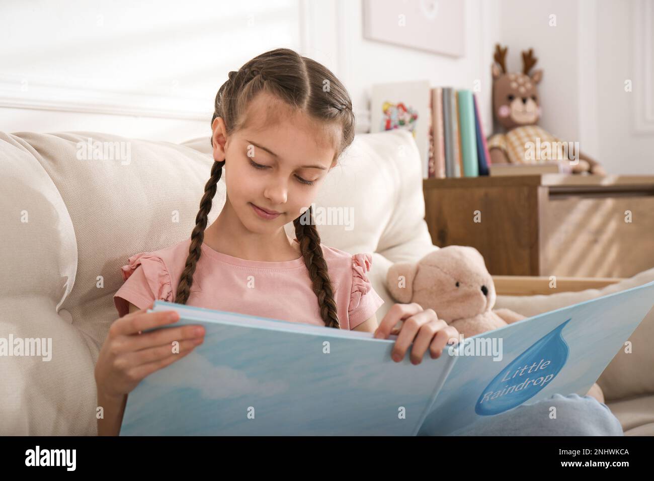 Cute little girl reading book on sofa at home Stock Photo - Alamy