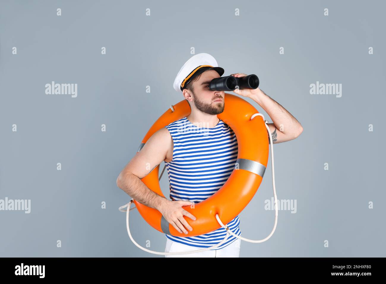 Sailor with binoculars and ring buoy on light grey background Stock Photo