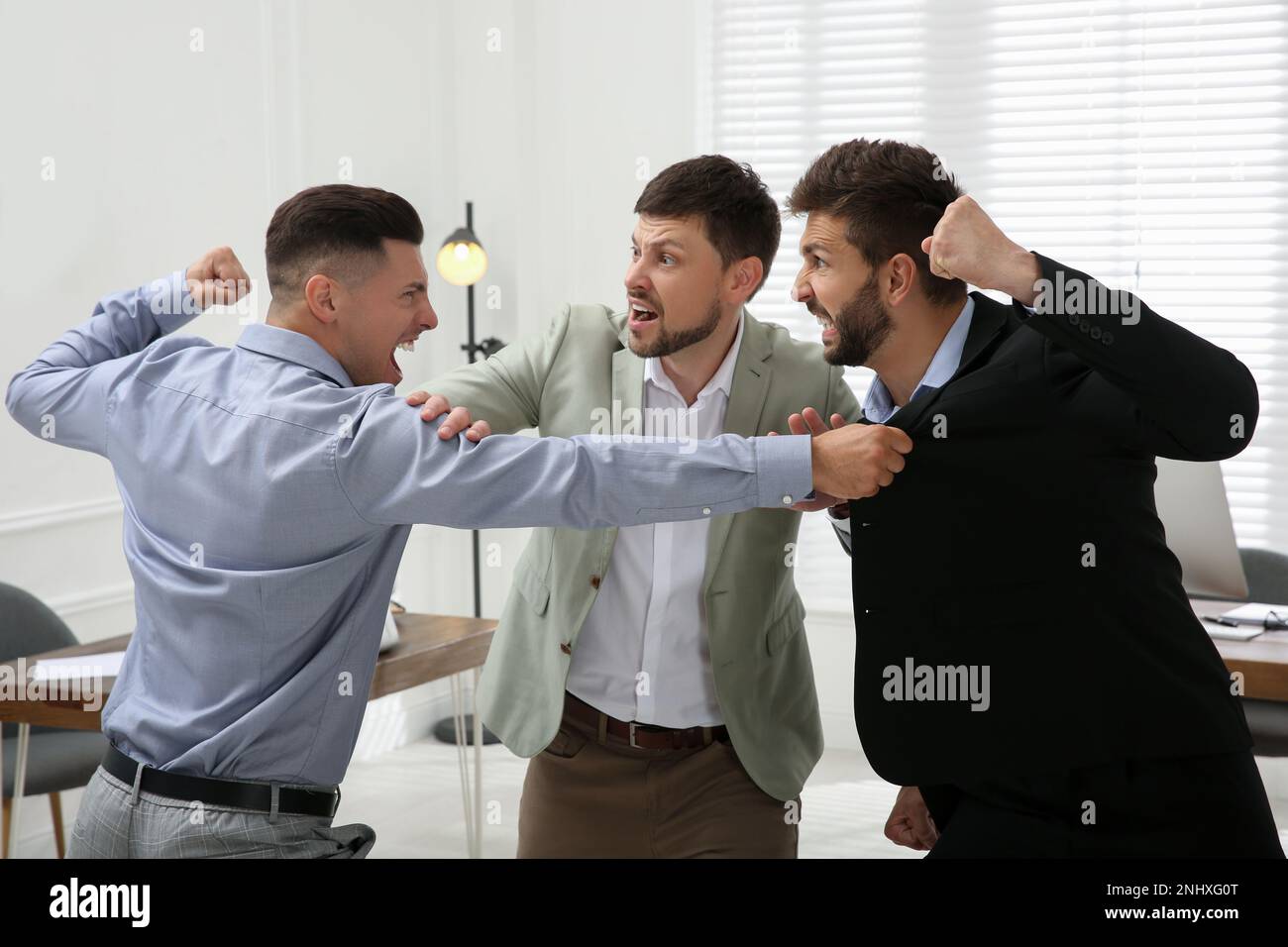 Man interrupting colleagues fight at work in office Stock Photo