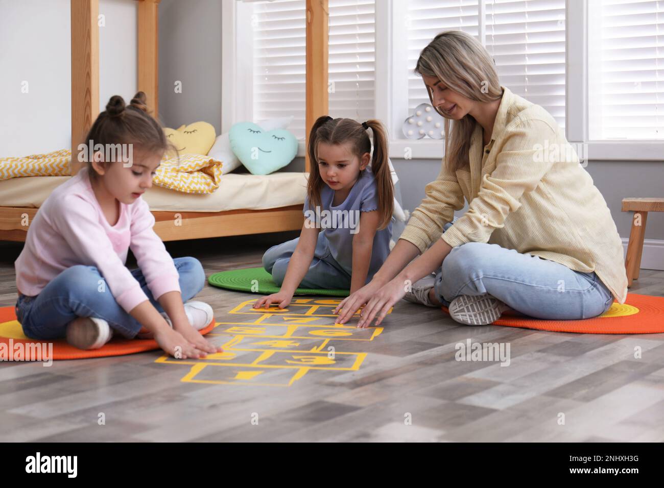Mother and little girls taping sticker hopscotch on floor at home Stock Photo