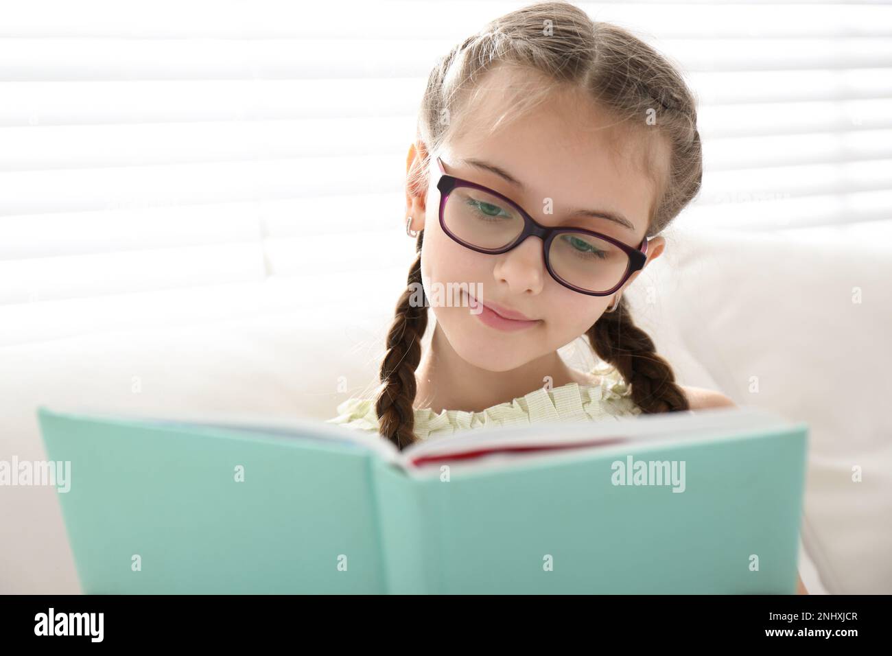 Cute little girl reading book near window at home Stock Photo - Alamy