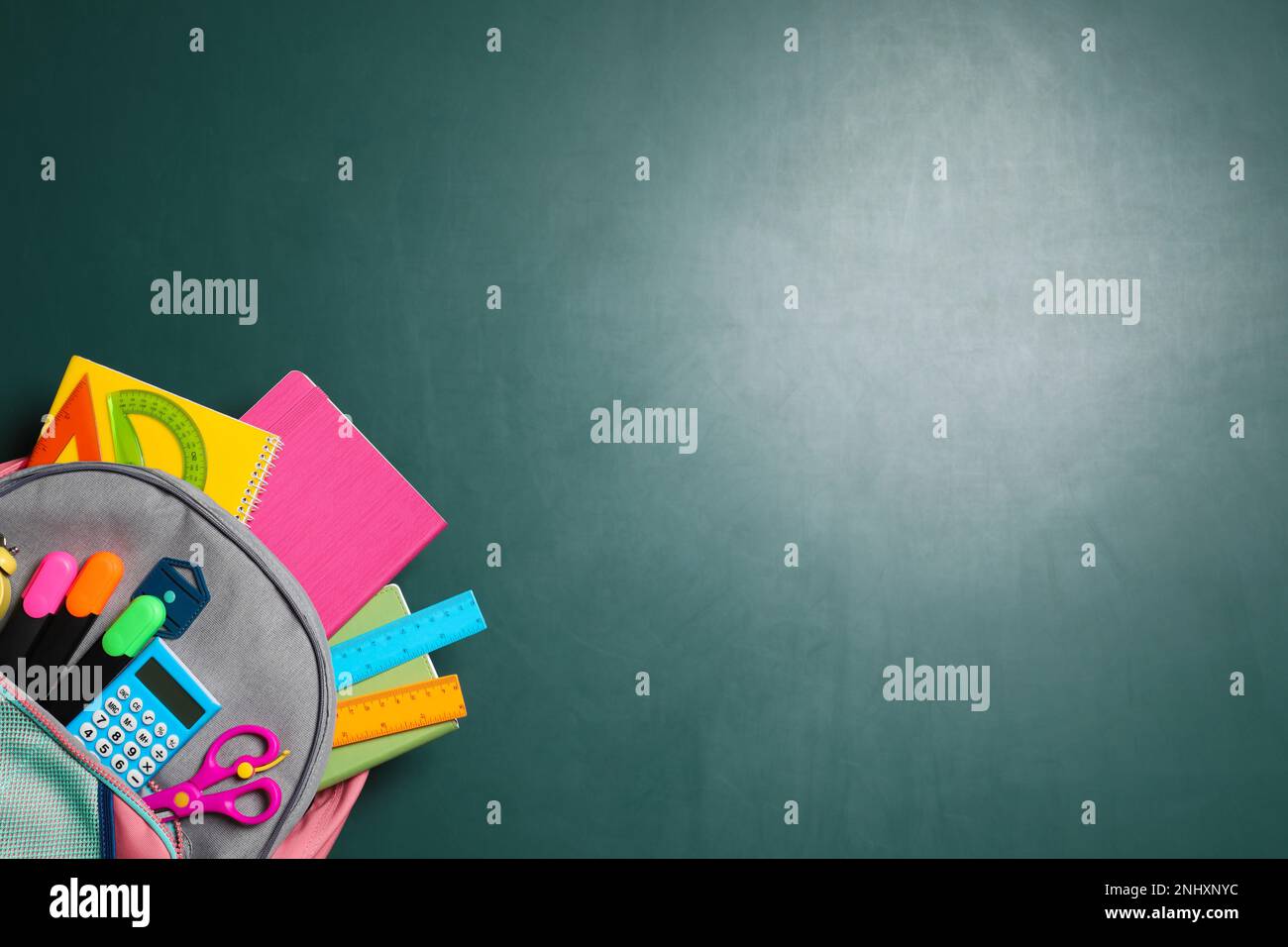 Backpack with different stationery on chalkboard background, top view. Space for text Stock Photo