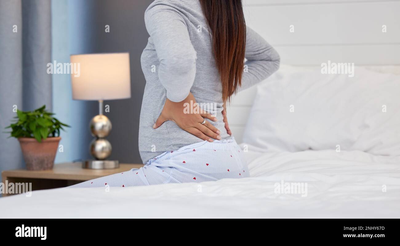 Tired, feeling and pregnant woman with back pain on a bed for rest, injury and fatigue