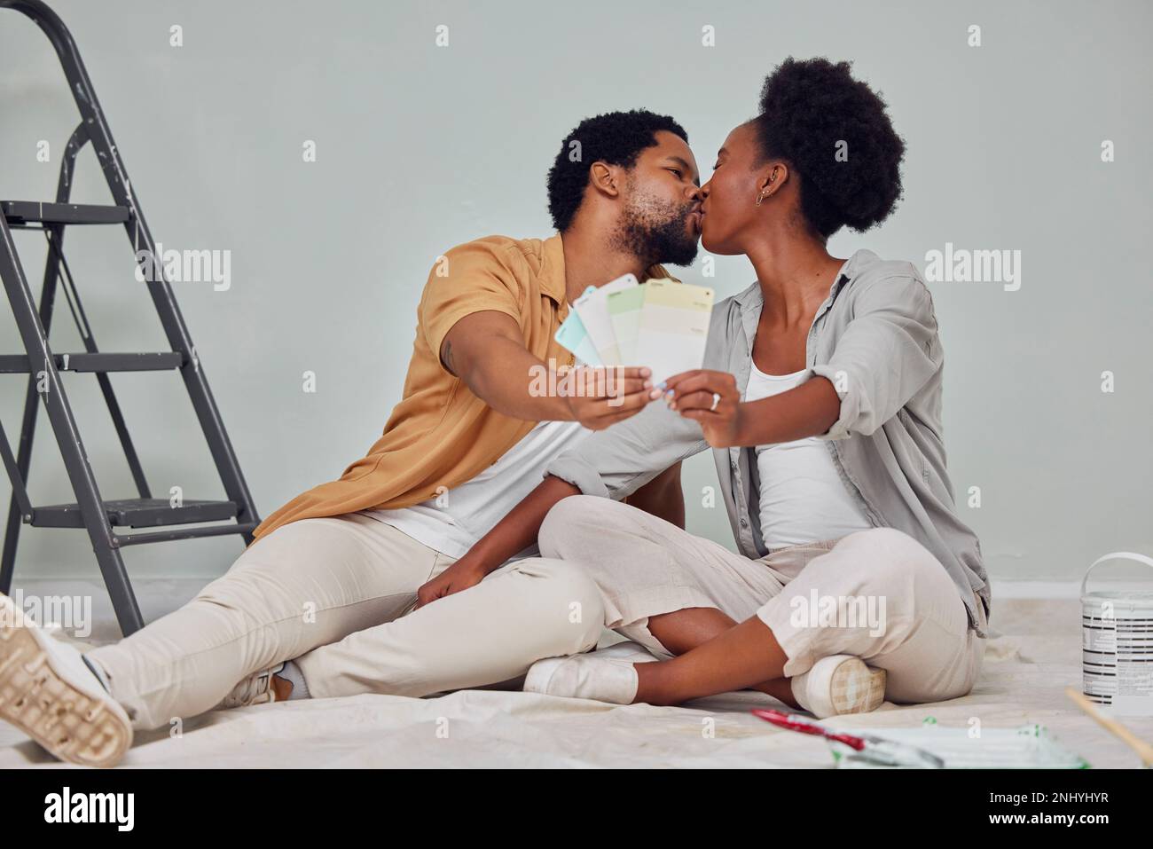 Painting color, love or black couple kiss in home renovation, diy or house remodel together by apartment ladder. Design, choices or African man Stock Photo
