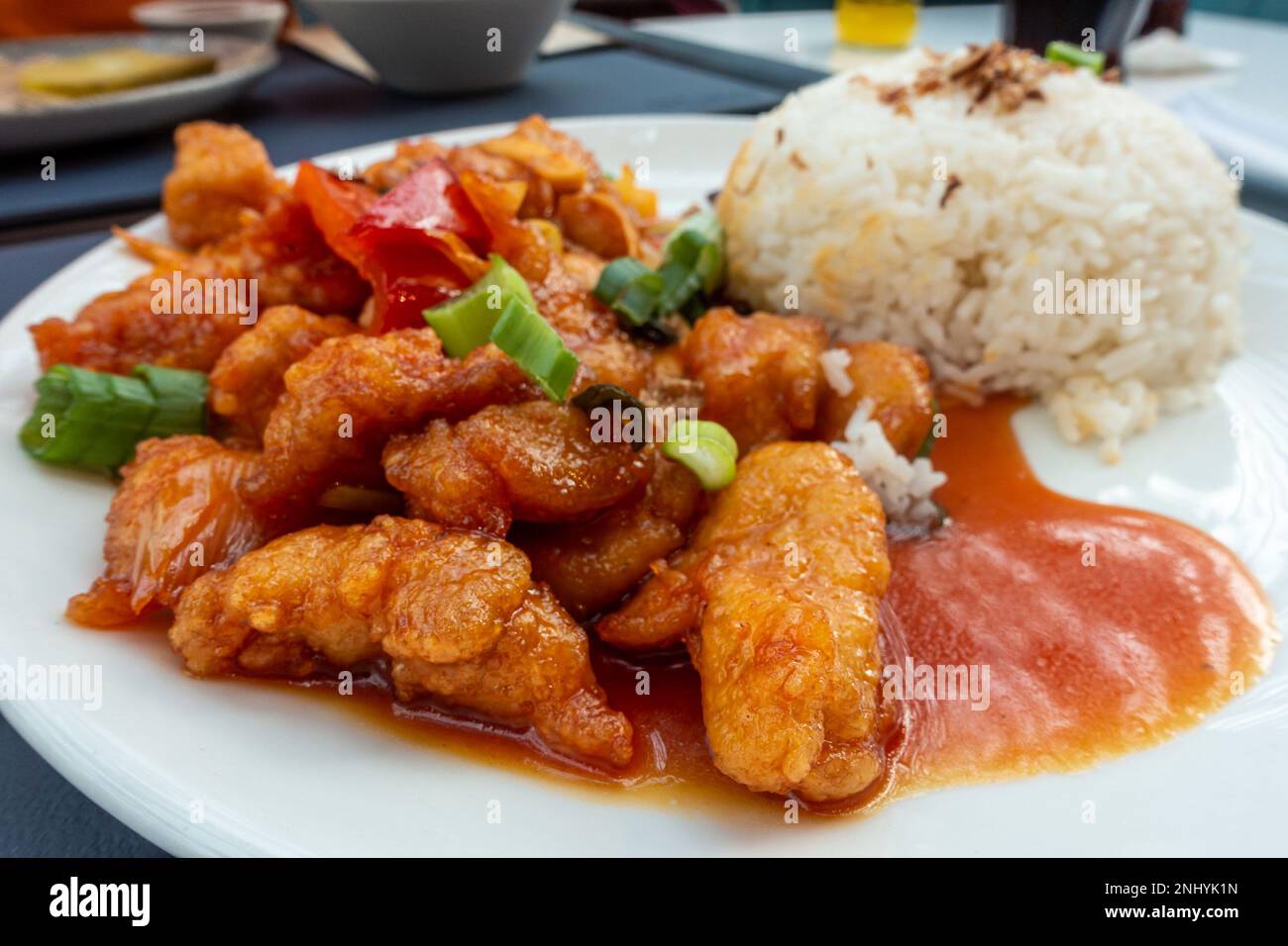 A plate of sweet and sour chicken with boiled rice, a Chinese inspired food served in a UK food court. Stock Photo