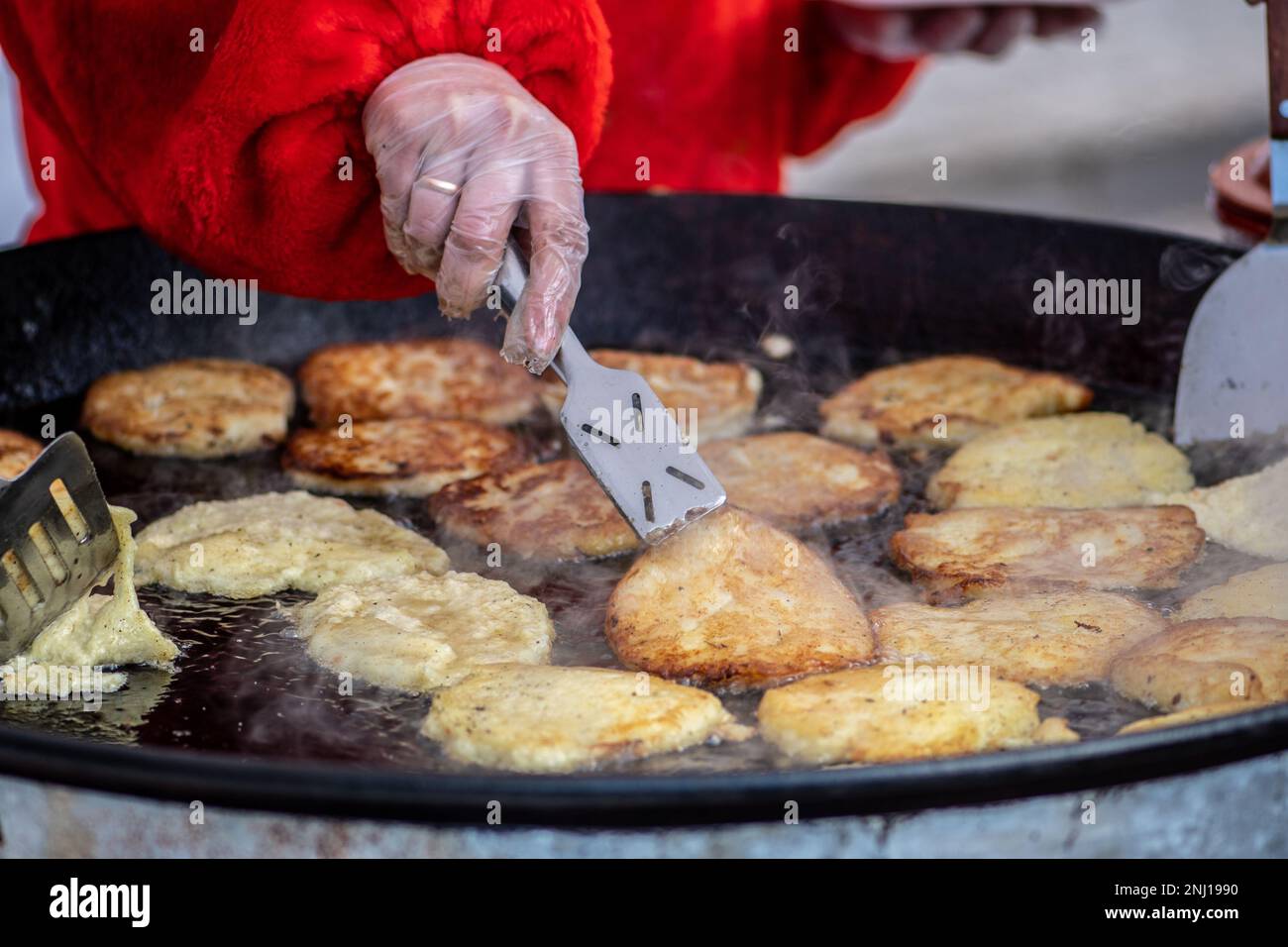 Frying traditional blini, blin or bulviniai blynai, potato pancakes on an open fire in a street food market Stock Photo