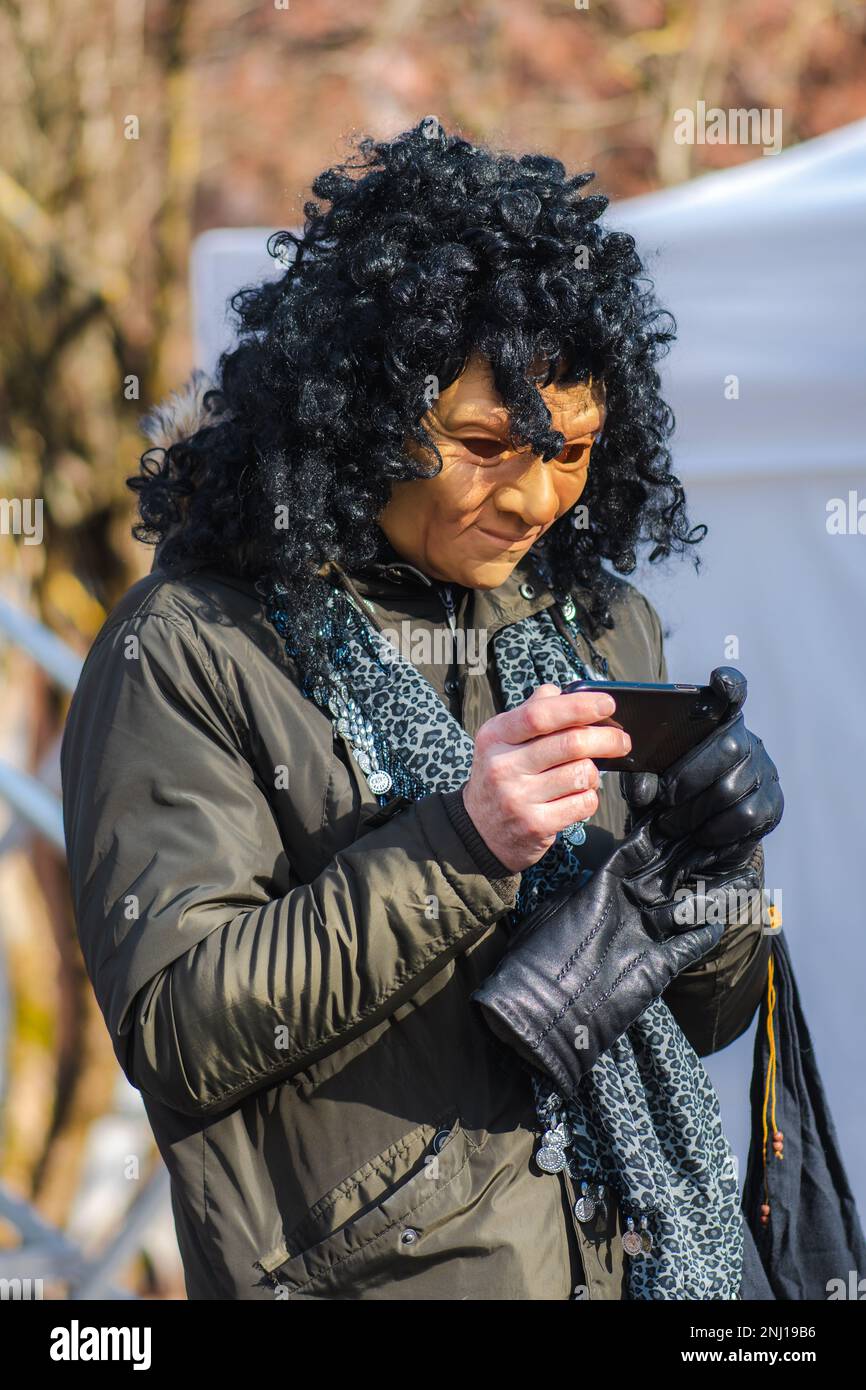 Man looking at the smartphone with an ugly scary mask during Uzgavenes, a Lithuanian folk festival during Carnival, seventh week before Easter Stock Photo