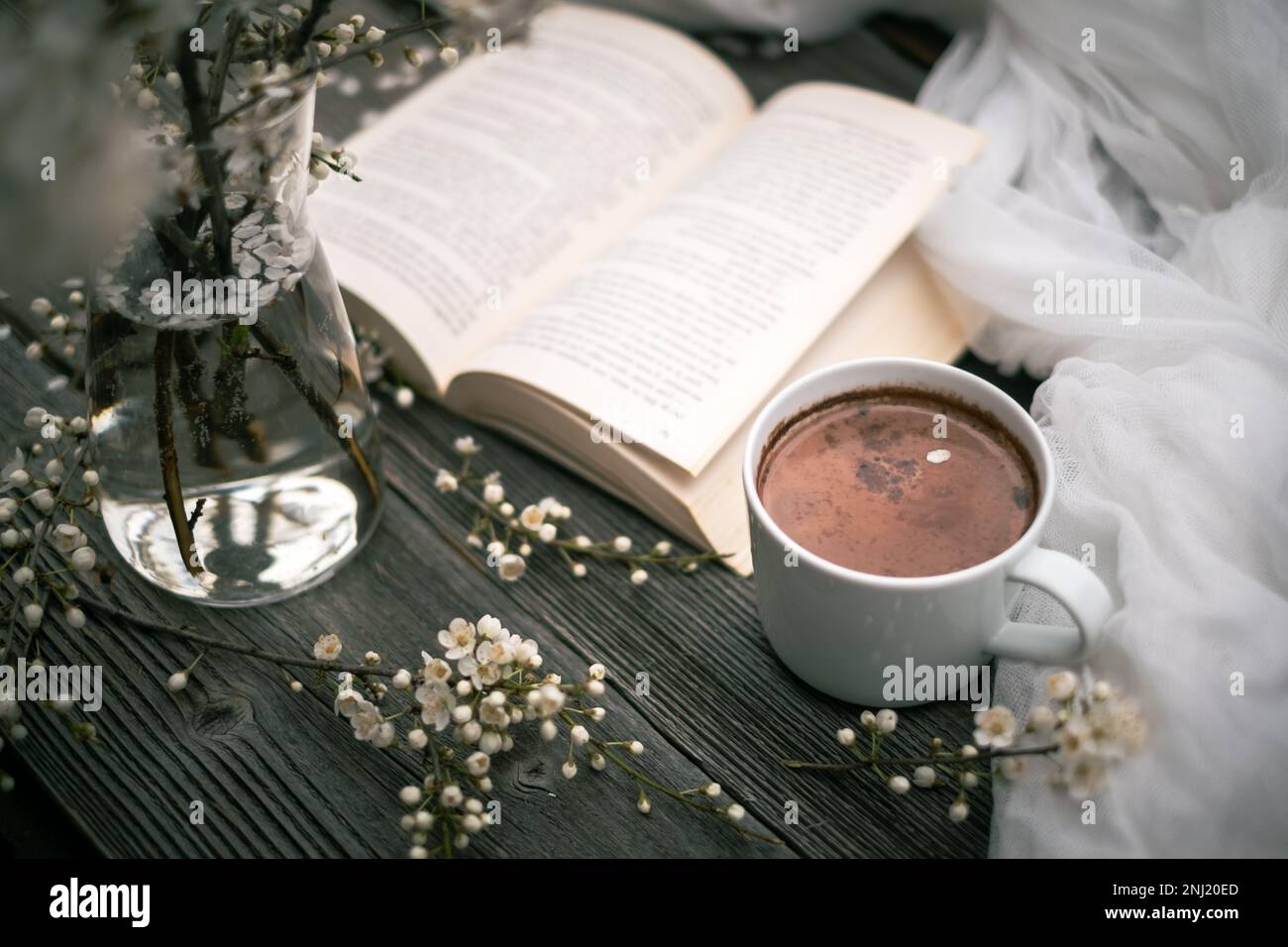 Cup of hot chocolate cacao, old book and spring cherry flowers on wooden background. Reading concept Stock Photo