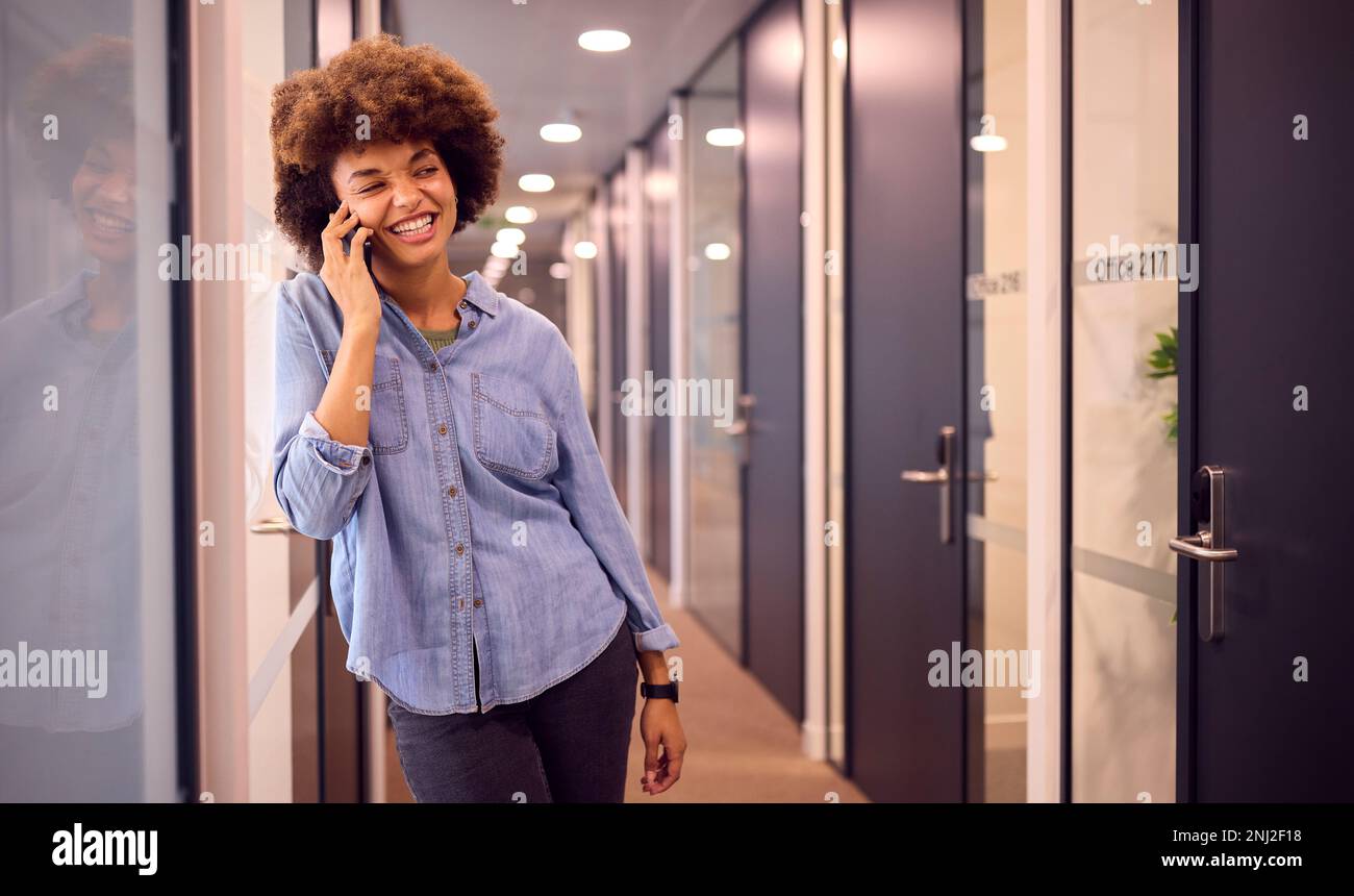 Smiling Young Businesswoman In Corridor Of Modern Office Talking On Phone Stock Photo